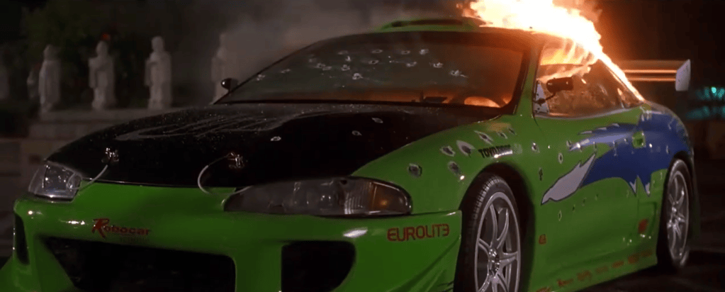 A green sports car with a black hood and blue graphics, showing visible bullet holes and flames emerging from the rear.